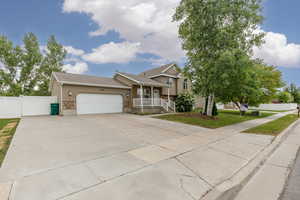 Tri-level home featuring stone siding, an attached garage, covered porch, stucco siding, and concrete driveway