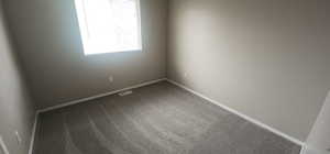 Spare room featuring visible vents, baseboards, and dark carpet
