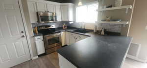 Kitchen featuring a sink, stainless steel appliances, wood finished floors, open shelves, and dark countertops