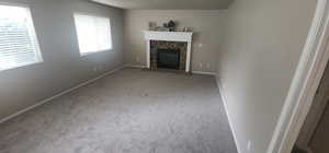 Unfurnished living room featuring baseboards, a stone fireplace, and carpet floors