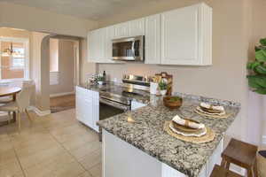 Kitchen featuring stainless steel appliances, a peninsula, white cabinets, light stone countertops, and arched walkways