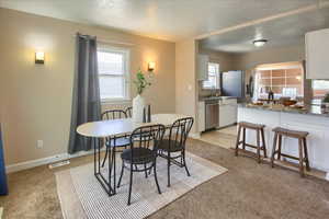 Dining room with a textured ceiling, light carpet, and baseboards