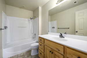 Bathroom with toilet, shower / tub combination, stone finish floor, visible vents, and vanity