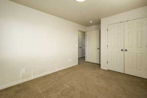 Unfurnished bedroom with a closet, light carpet, and baseboards