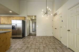 Kitchen with stone finish flooring, a chandelier, a towering ceiling, and stainless steel refrigerator.