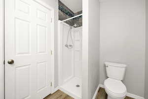 Bathroom with wood finished floors, walk in shower, baseboards, and toilet