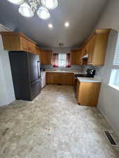 Kitchen with freestanding refrigerator, under cabinet range hood, visible vents, a sink, and light countertops