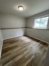 Empty room with a textured ceiling, wood finished floors, and baseboards