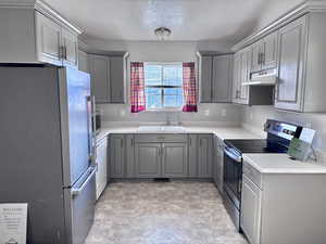 Kitchen with stainless steel appliances, gray cabinets, light countertops, a textured ceiling, and under cabinet range hood