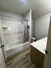 Bathroom with vanity, shower / bath combo, toilet, and wood finished floors