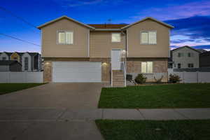 Raised ranch with fence, brick siding, a garage, concrete driveway, and a yard