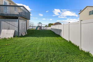 View of yard with a deck, a fenced backyard, a shed, a playground, and an outbuilding