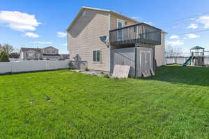 Back of house featuring a yard, fence, a wooden deck, and a playground
