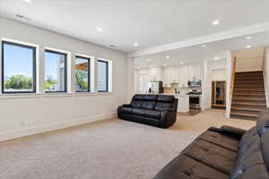 Living room with light colored carpet, visible vents, recessed lighting, stairway, and baseboards
