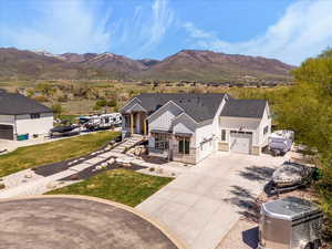 View of front of property featuring a mountain view, driveway, stone siding, a front lawn, and board and batten siding