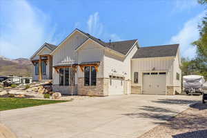 View of front of property with stone siding, board and batten siding, driveway, and a garage