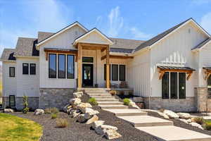 View of front of home with board and batten siding, roof with shingles, and stone siding