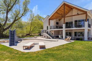 Rear view of property featuring stairway, a balcony, a patio, and a lawn