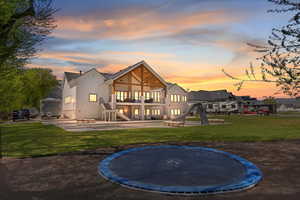 Back of property at dusk featuring a patio area, a trampoline, a balcony, stairway, and a lawn