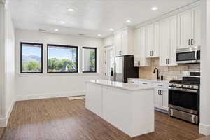 Kitchen with stainless steel appliances, tasteful backsplash, light countertops, a center island, and baseboards