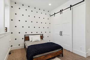 Bedroom with baseboards, recessed lighting, light carpet, and a barn door