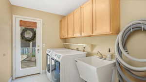 Laundry area with light tile patterned floors, cabinet space, a sink, and washer and clothes dryer