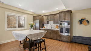 Kitchen featuring dark brown cabinetry, appliances with stainless steel finishes, decorative backsplash, and light wood-style flooring
