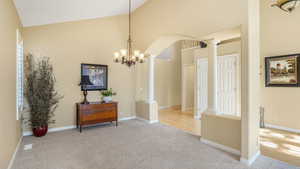 Interior space featuring carpet flooring, an inviting chandelier, decorative columns, high vaulted ceiling, and arched walkways