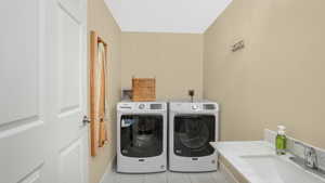 Laundry room with washing machine and clothes dryer, laundry area, light tile patterned floors, and a sink