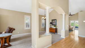 Corridor featuring baseboards, high vaulted ceiling, a notable chandelier, and decorative columns