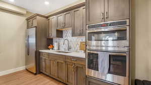 Kitchen featuring a sink, stainless steel appliances, light wood-type flooring, decorative backsplash, and baseboards