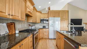 Kitchen featuring light wood finished floors, a sink, dark stone counters, stainless steel appliances, and vaulted ceiling