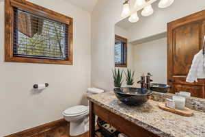 Half bath with toilet, wood finished floors, baseboards, vaulted ceiling, and vanity