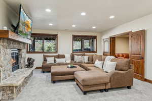 Carpeted living room with baseboards, a stone fireplace, and recessed lighting