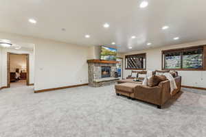 Living room featuring a stone fireplace, carpet floors, baseboards, and recessed lighting
