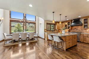 Kitchen featuring dark wood finished floors, custom exhaust hood, high end stove, decorative backsplash, and a center island
