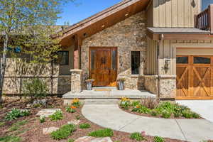 Entrance to property featuring a garage, stone siding, and board and batten siding