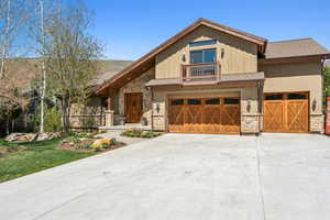View of front of house featuring an attached garage, stone siding, driveway, board and batten siding, and a shingled roof