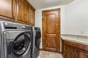 Clothes washing area with cabinet space, washer and clothes dryer, and a textured ceiling