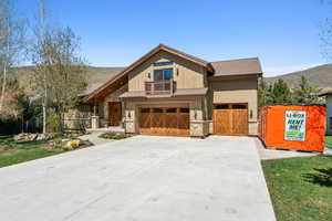 View of front of house with driveway, a mountain view, an attached garage, stone siding, and roof with shingles