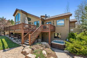 Rear view of house featuring a hot tub, stucco siding, a shingled roof, stairway, and a wooden deck
