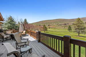 Wooden terrace featuring a yard, golf course view, outdoor dining area, and a mountain view