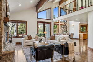 Living area with wood finished floors, baseboards, a stone fireplace, and high vaulted ceiling