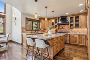 Kitchen featuring glass insert cabinets, custom exhaust hood, high end range, dark wood finished floors, and a kitchen island