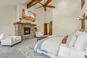 Carpeted bedroom featuring beam ceiling, a fireplace, ceiling fan, and high vaulted ceiling