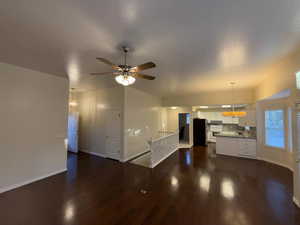Unfurnished living room featuring dark wood-style flooring, a ceiling fan, and baseboards