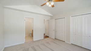 Unfurnished bedroom with ceiling fan, carpet floors, two closets, baseboards, and vaulted ceiling