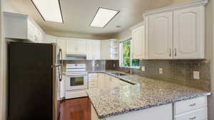 Kitchen featuring open shelves, a sink, white appliances, a peninsula, and under cabinet range hood