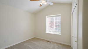 Spare room featuring visible vents, lofted ceiling, light carpet, baseboards, and ceiling fan