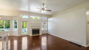 Unfurnished living room featuring ceiling fan, visible vents, a tiled fireplace, wood finished floors, and baseboards